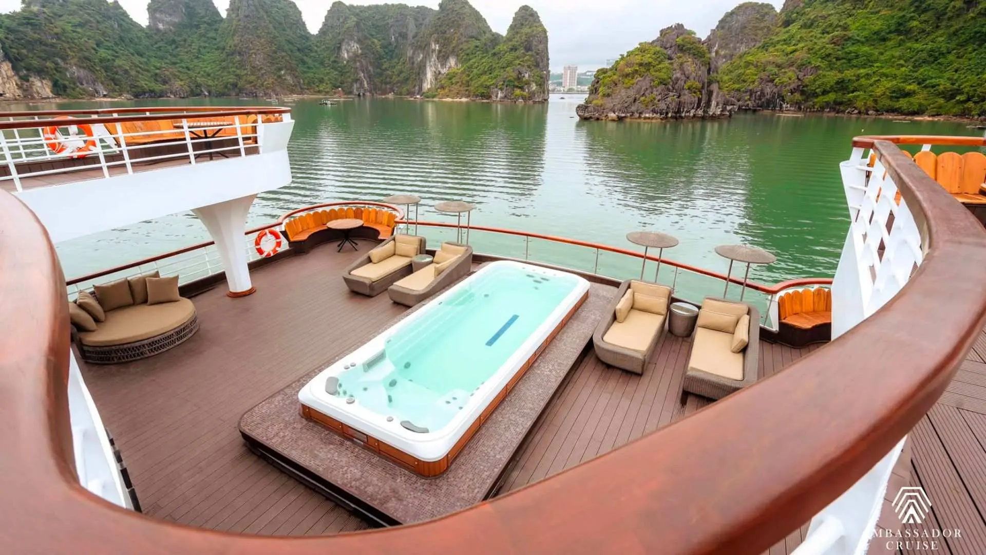 Open-air deck of the Ambassador luxury cruise in Halong Bay, featuring a long jacuzzi, comfortable sun loungers, and seating for ultimate relaxation amidst scenic views.