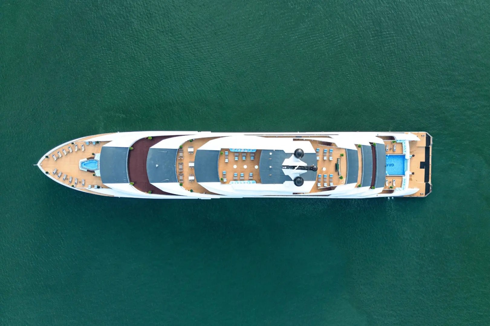 Top-down aerial view of the Ambassador luxury 5-star day cruise ship, highlighting its multiple spacious decks and sleek design as it navigates Halong Bay's emerald waters.