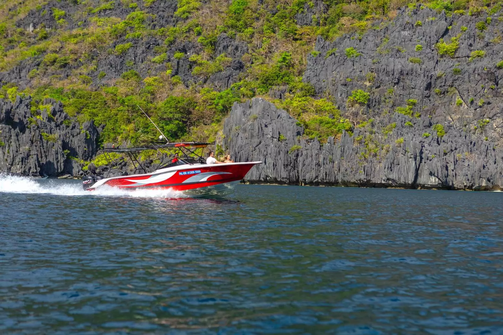 Seaction luxury speedboat speeding past lush green limestone cliffs in El Nido, Philippines, exploring hidden lagoons and pristine beaches of Palawan, creating white water splashes.