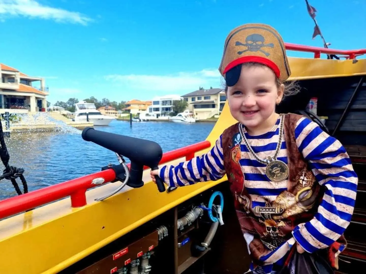 A happy young girl in a pirate costume operating a water cannon on the Mandurah Pirate Cruise, enjoying the fun canal adventure experience.