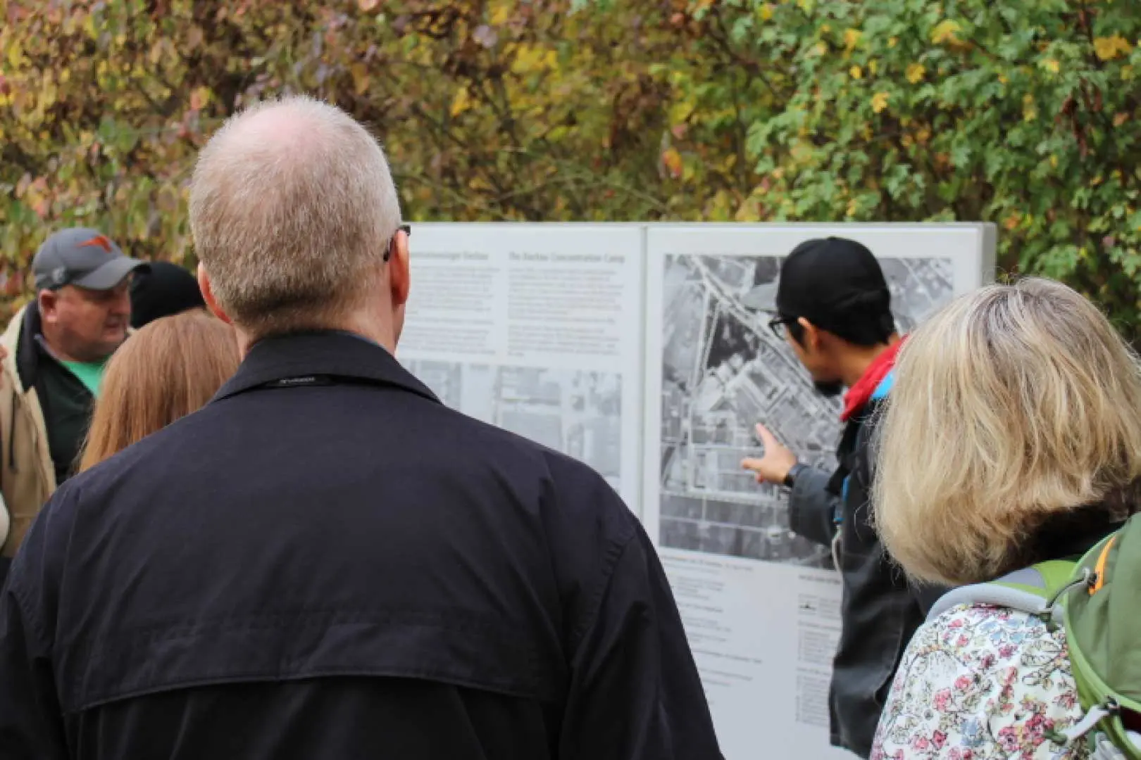 Visitors at Dachau Concentration Camp Memorial Site intently examining historical information boards under the guidance of a tour guide, learning about the details of the Holocaust and camp history.