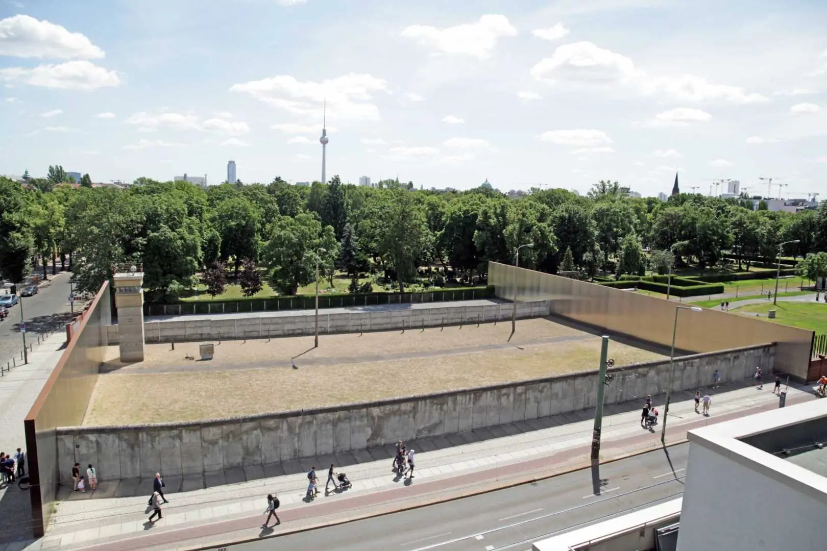 Panoramic view of the Berlin Wall Memorial in East Berlin, showing reconstructed wall sections, a wide 'death strip,' and the historic TV Tower in the background, highlighting the communist era's impact.