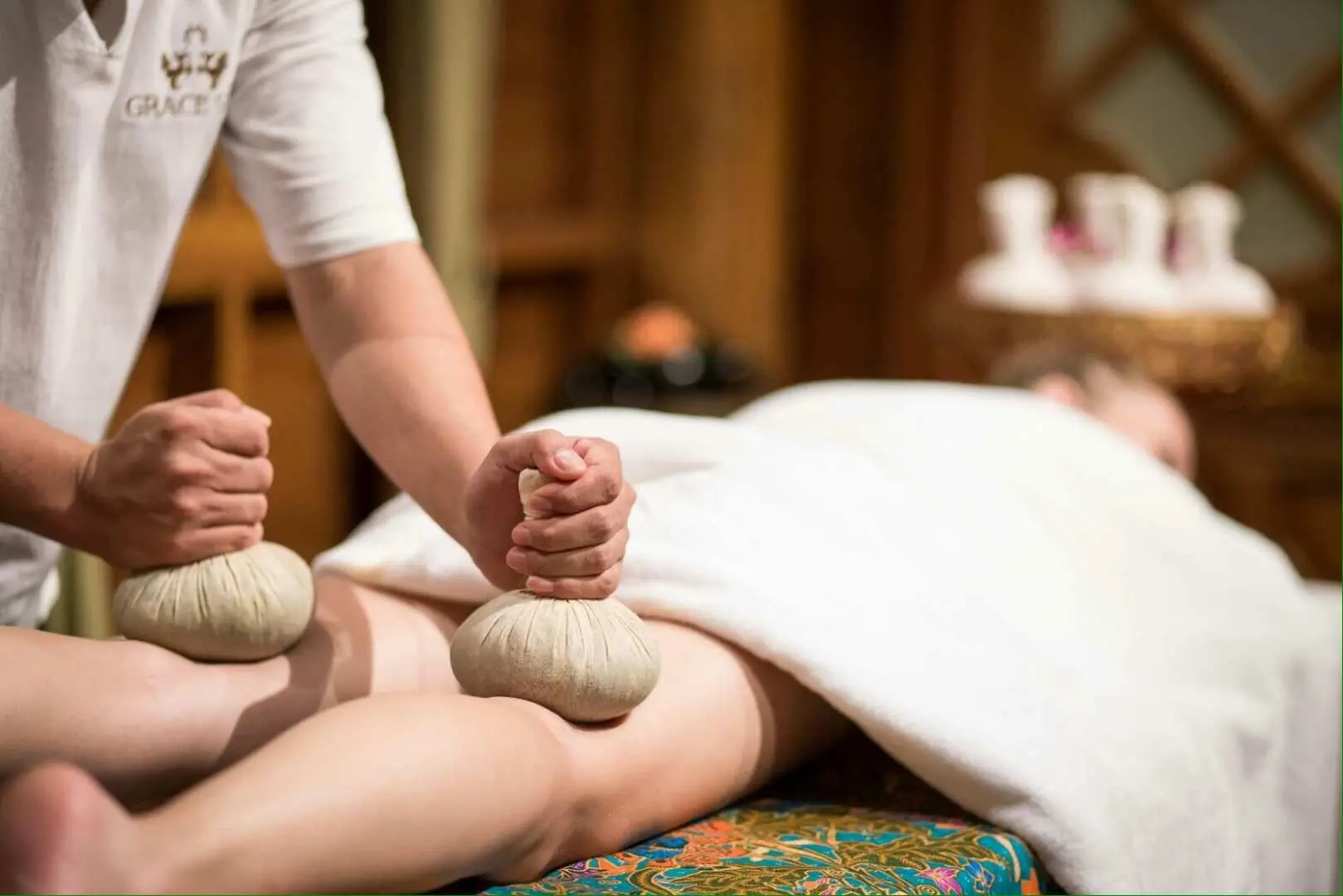 Therapist applies warm herbal compresses to a client's legs at Grace Spa Pattaya, promoting deep relaxation and blood circulation with traditional Thai therapy.