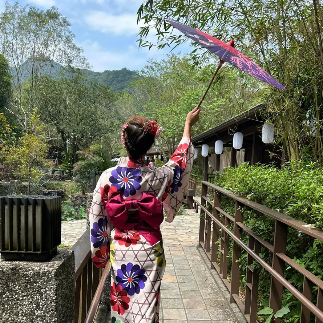 身著亮麗花卉浴衣的旅客，手持日式油紙傘，漫步於礁溪森林風呂的木棧道上，享受群山環繞的自然美景與和服體驗。