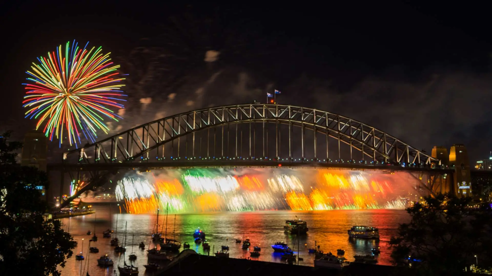 Colorful 2026 New Year's Eve fireworks bursting above Sydney Harbour Bridge, accompanied by a vibrant bridge light show, illuminating the iconic Sydney Harbour at night.