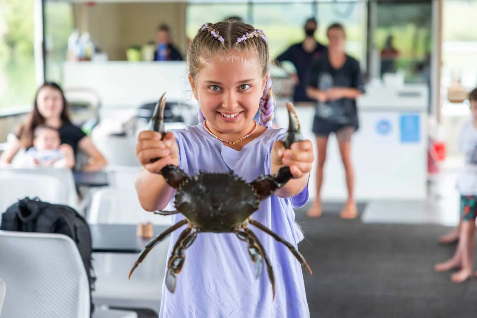 A cheerful young girl on the Tweed River crab catching tour proudly displays a live mud crab she personally caught, showcasing a delightful moment of family-friendly hands-on experience.