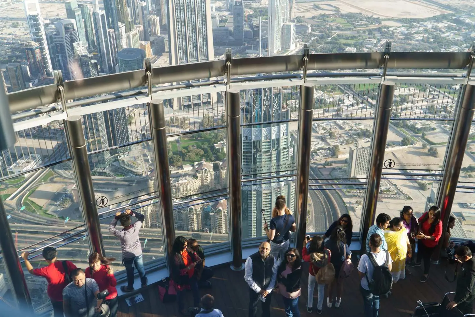 High-angle view from Burj Khalifa observation deck, with visitors enjoying the breathtaking panoramic cityscape of modern Dubai spread out below.