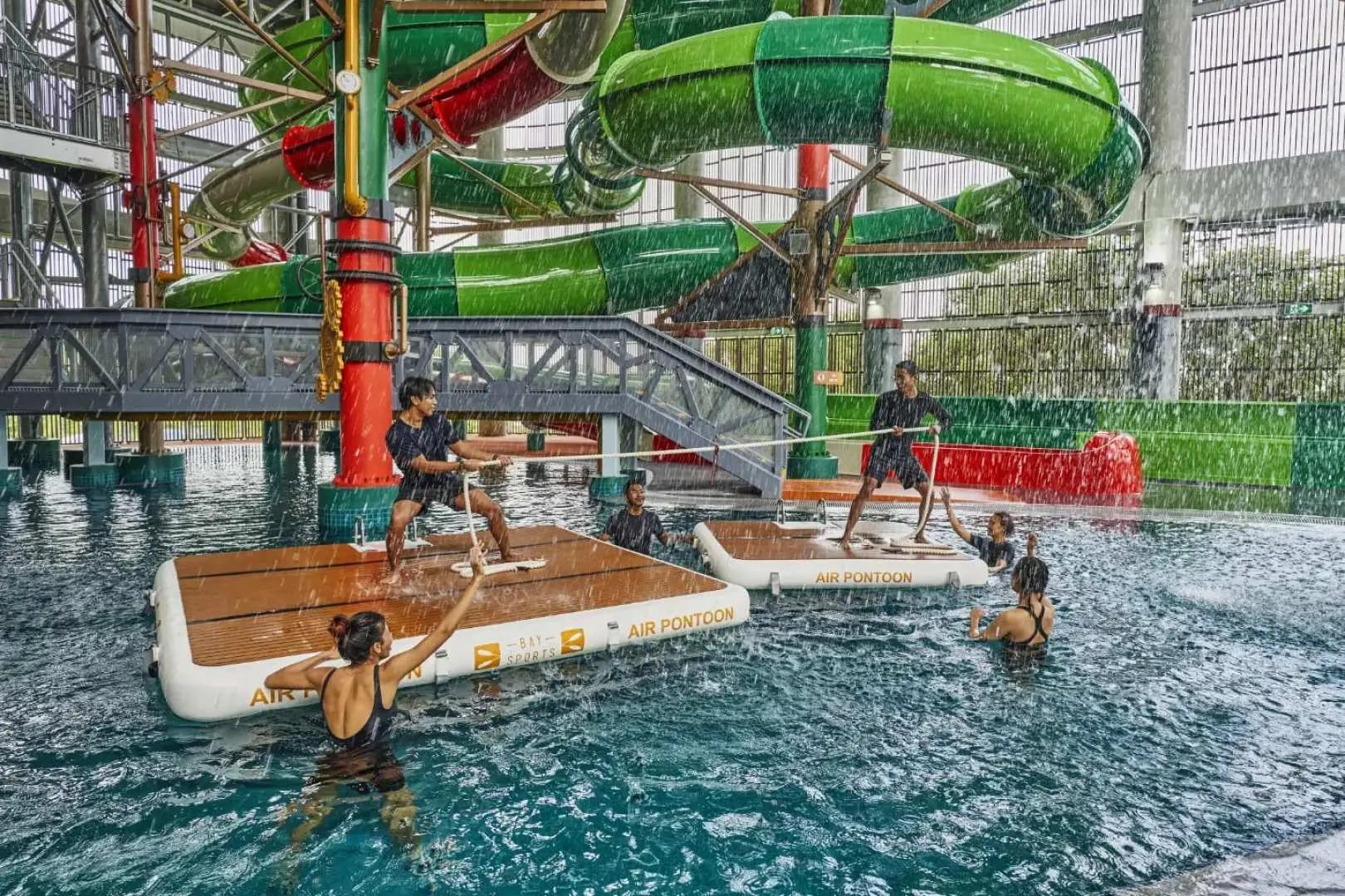 Visitors enjoying the indoor water floating challenge at HomeTeamNS Bedok Reservoir Aqua Adventure in Singapore, navigating inflatable pontoons in the pool as an interactive obstacle game.
