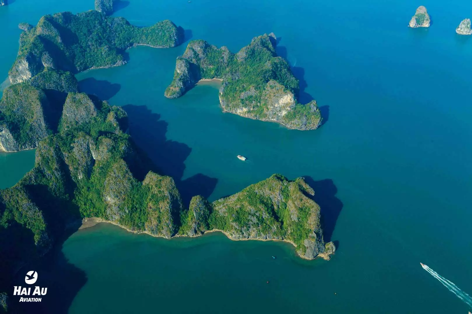 水上飞机上俯瞰广阔的下龙湾，翠绿石灰岩岛屿绵延，湛蓝海面上有船只航行，展现壮丽自然奇景。