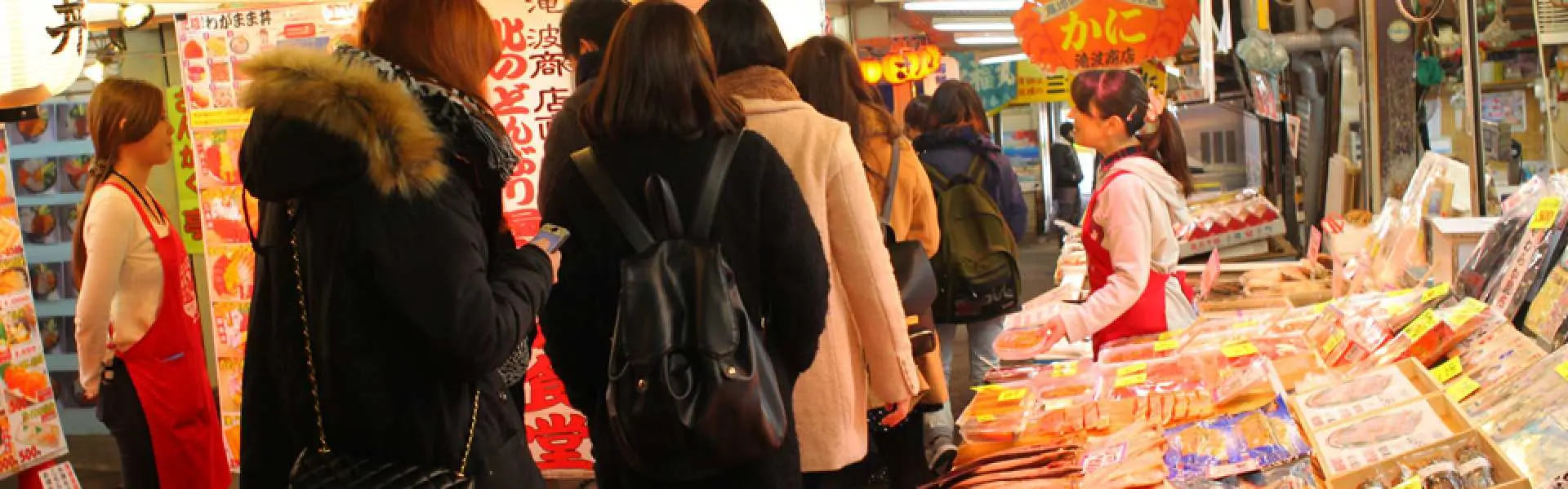 A bustling indoor seafood market in Otaru, Hokkaido, with visitors navigating various stalls filled with fresh seafood, offering a rich local culinary experience on a private guided tour.