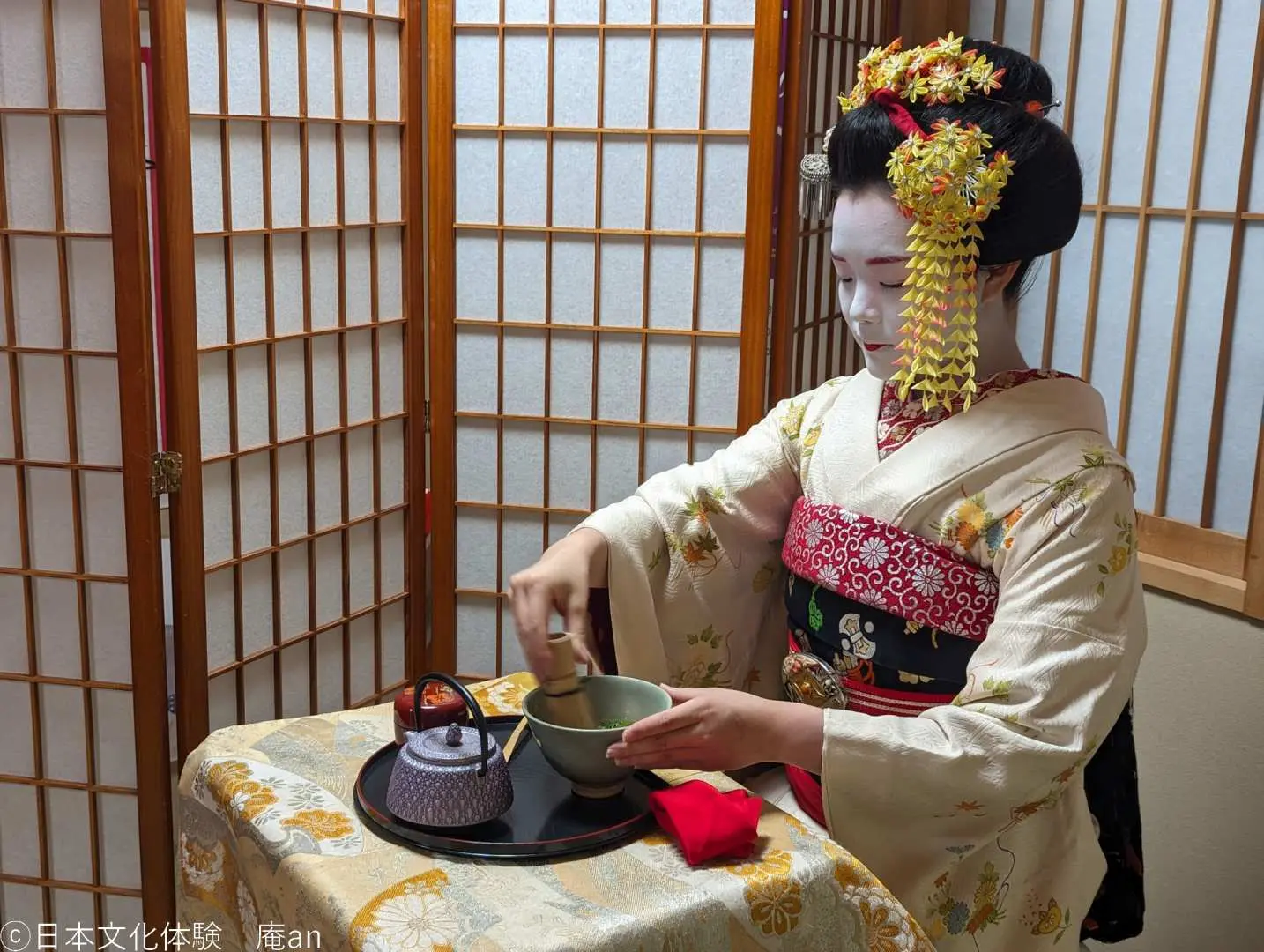 京都舞妓穿著精緻和服，在日式傳統空間內專注地進行茶道表演，展現優雅文化。