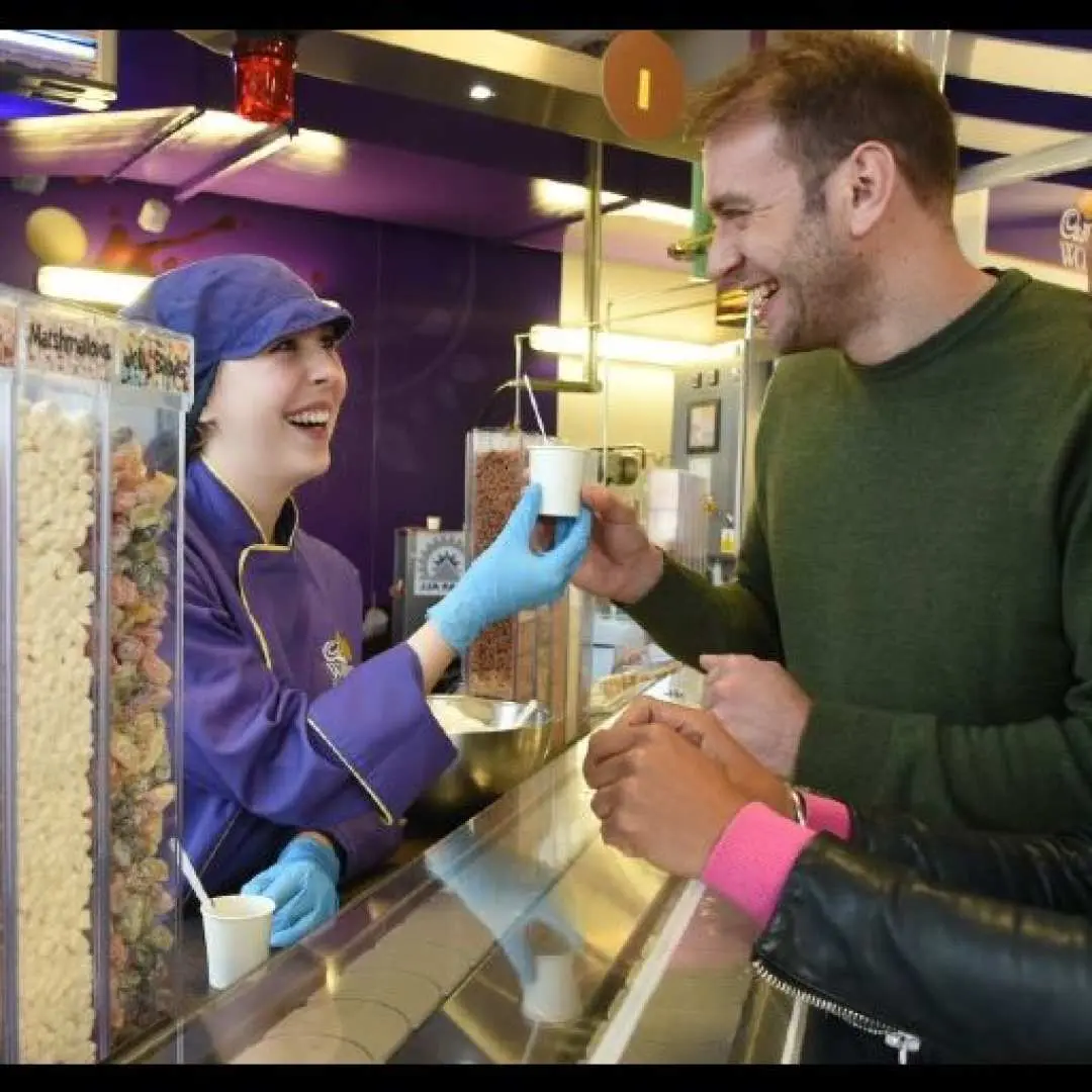 A smiling visitor receives a delicious chocolate sample from a friendly staff member in purple uniform at Cadbury World, Birmingham, enjoying a sweet interactive experience.