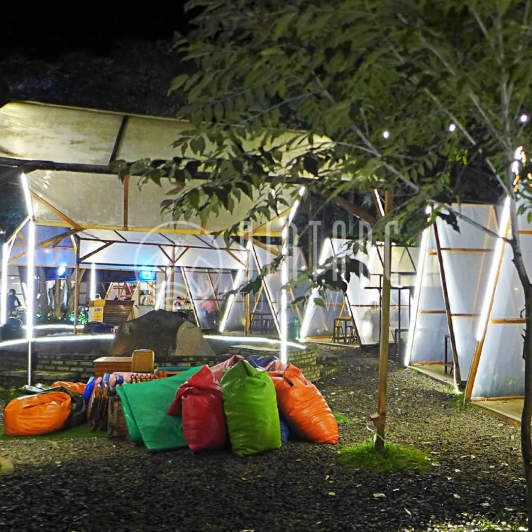 バンドンの活気ある夜の屋外リラックスエリア。光るテントとカラフルなビーズクッションがユニークで快適な雰囲気を醸し出しています。