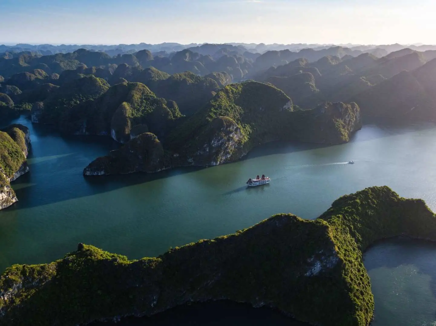 An aerial view of the magnificent karst landscape of Halong Bay and Lan Ha Bay, with the V'Spirit luxury cruise ship navigating through, offering an unforgettable Vietnamese nature adventure.
