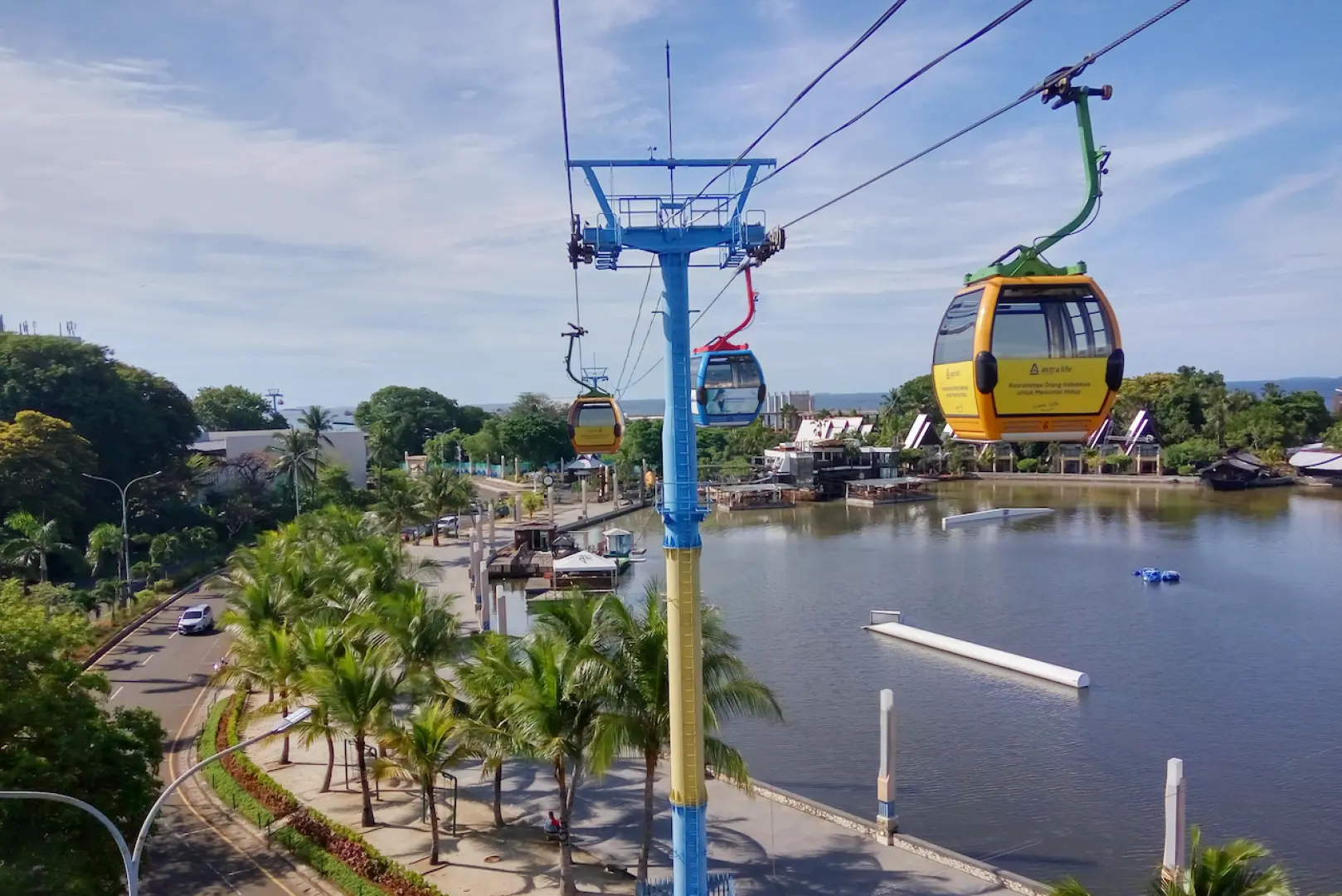 Ancol Cable Car cabins, vibrant yellow, soaring above a Jakarta bay and green resort landscape, offering panoramic aerial views of the Ancol Dreamland area.