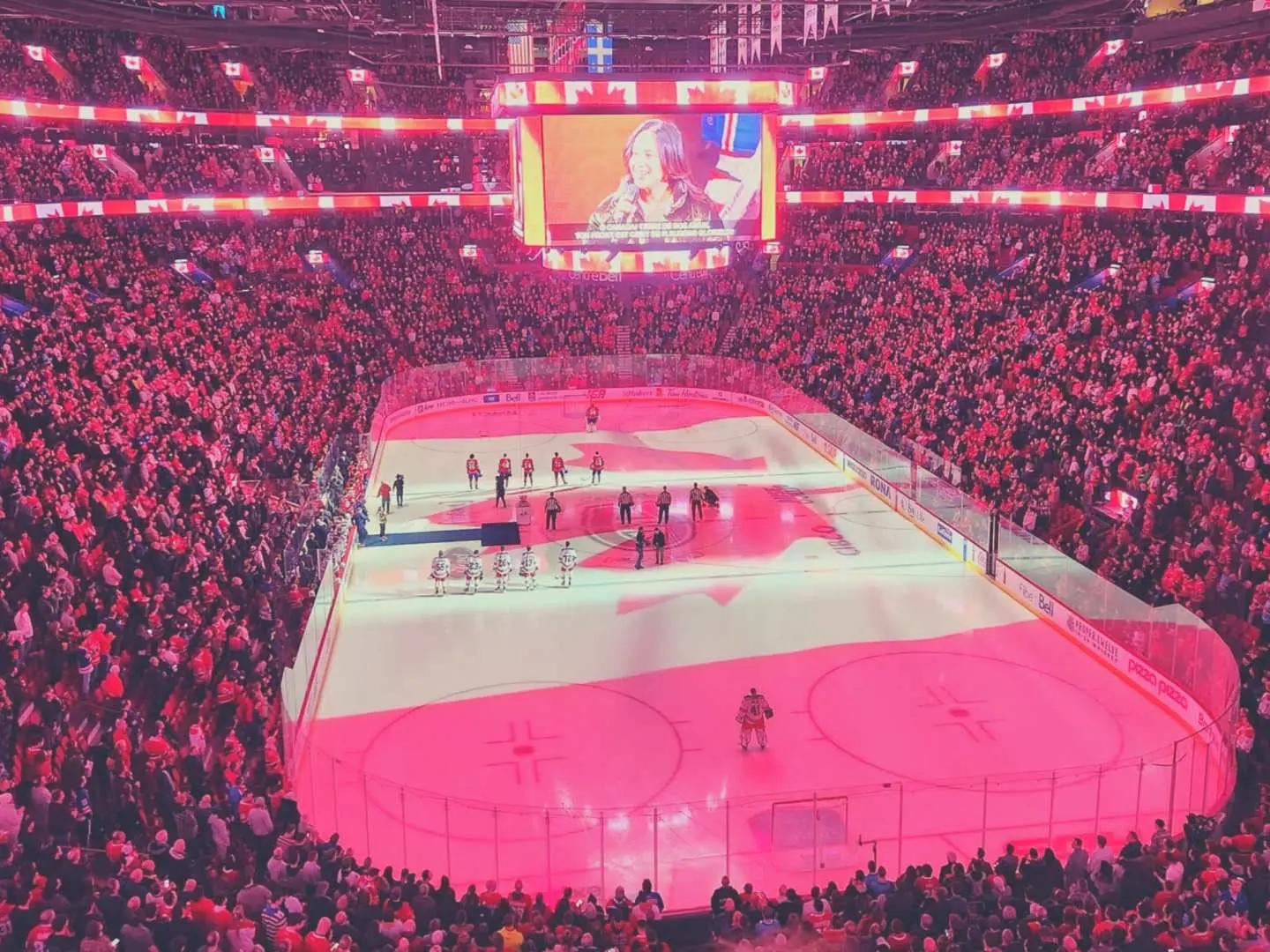 Bell Centre ice rink for a Montreal Canadiens NHL game, illuminated with a red Canadian flag or maple leaf projection, creating a patriotic atmosphere.