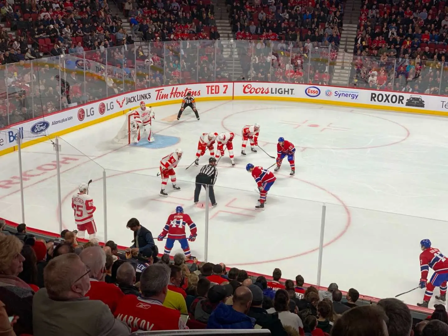 Close-up of a face-off during a Montreal Canadiens NHL game at Bell Centre, featuring players, a referee, and enthusiastic fans near the ice.