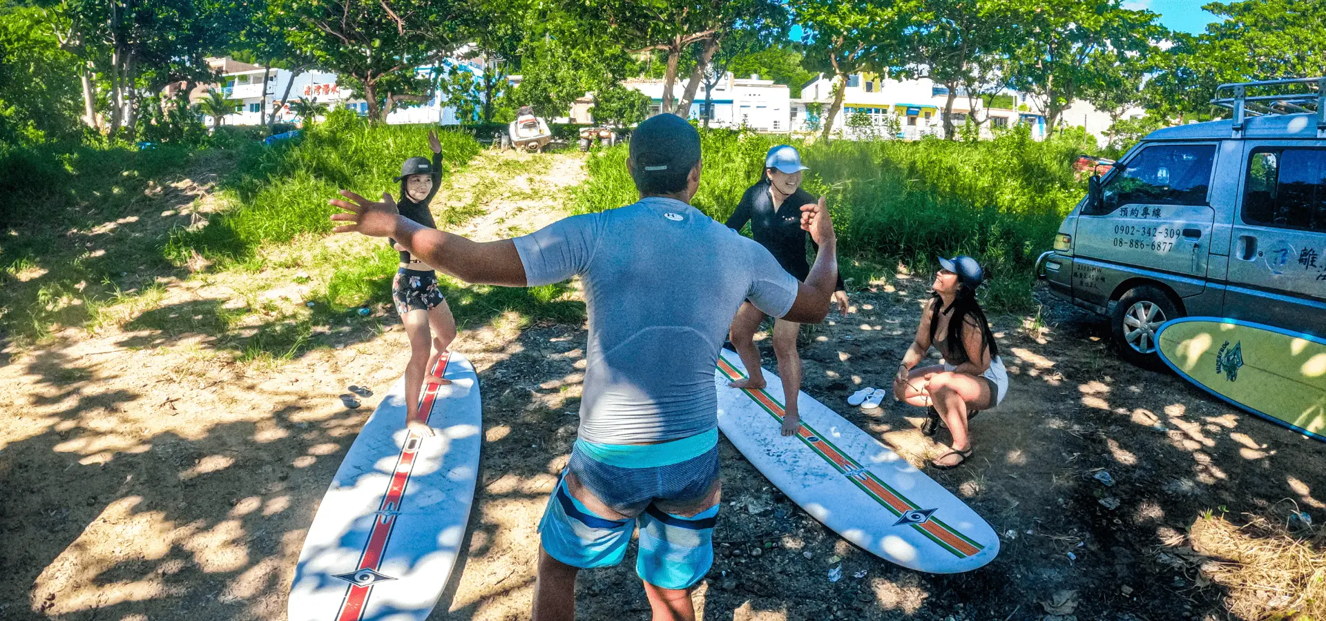 A surfing coach demonstrating proper stance to students on the sandy beach in Kenting, practicing before hitting the waves with stable surfboards.