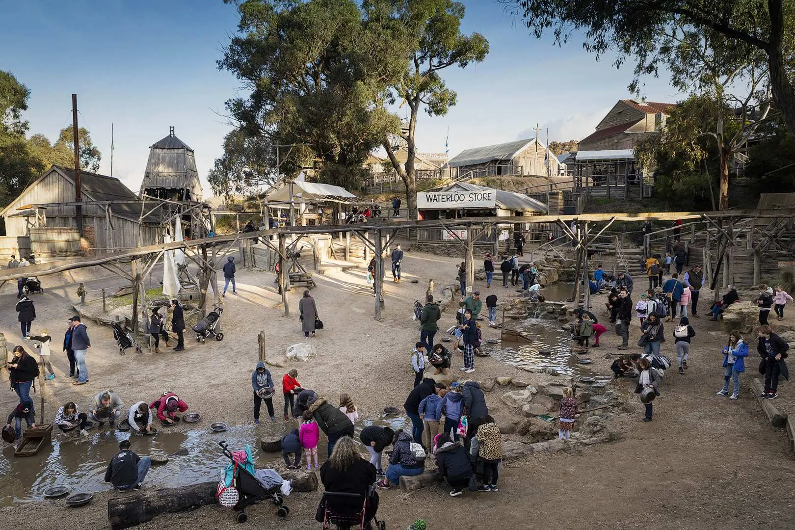 An overhead view of the bustling outdoor gold panning area at Sovereign Hill, showing numerous visitors actively sifting for gold in the water channels, recreating the gold rush.