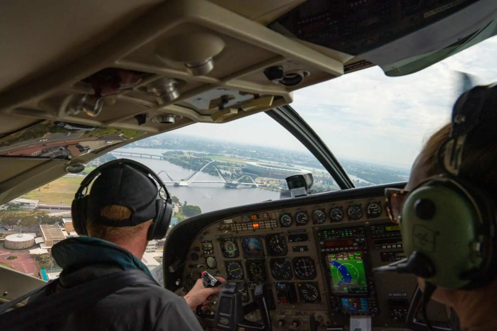 Inside the Perth seaplane cockpit, a pilot operates controls, offering aerial views of city landmarks like Matagarup Bridge.