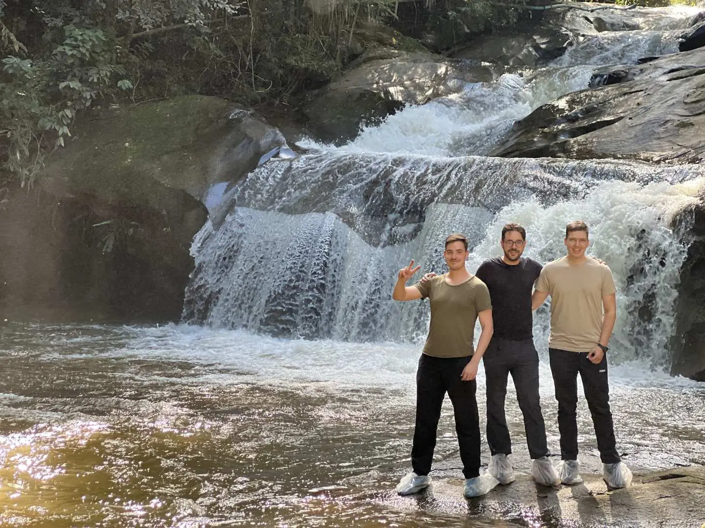 Three friends pose happily in front of a magnificent waterfall in Doi Inthanon National Park, enjoying the splashing water and the joy and vitality brought by nature.