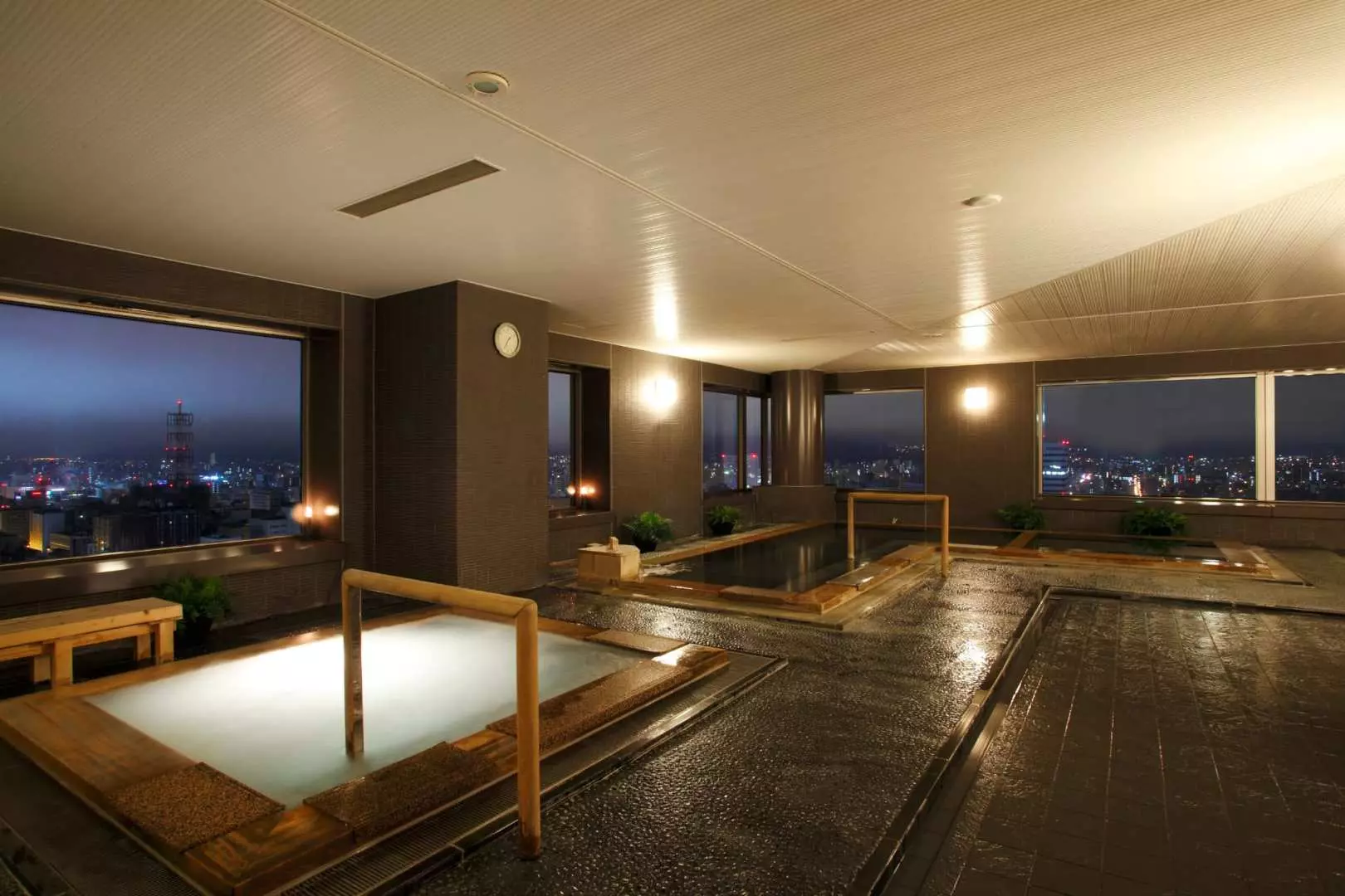 北海道札幌日航ホテルSKY RESORT SPAの天然温泉。木製の浴槽が夜に輝き、札幌の煌めく夜景を眼下に、特別な高層温泉を堪能。