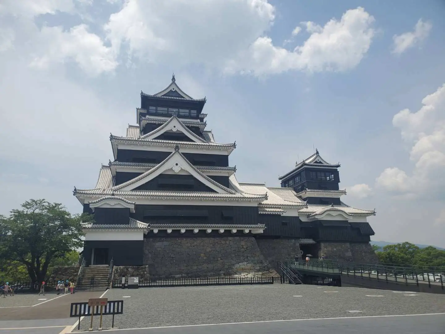 青空の下、雄大な熊本城天守閣がそびえ立ち、日本の戦国時代の建築様式と歴史的な威厳を示す。