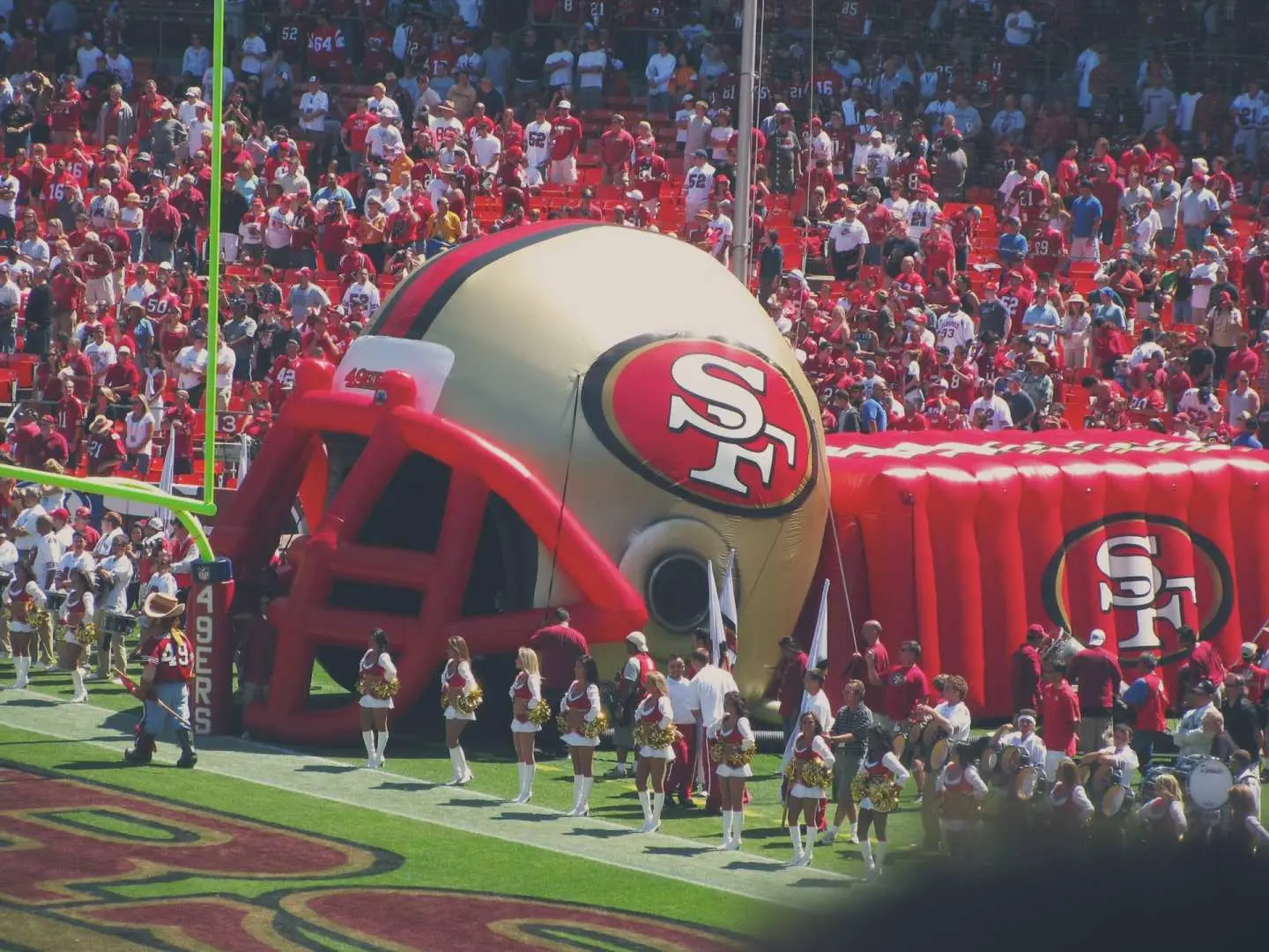 Inflatable San Francisco 49ers helmet tunnel and cheerleaders on the field during an NFL game at Levi's Stadium, energizing the enthusiastic crowd.