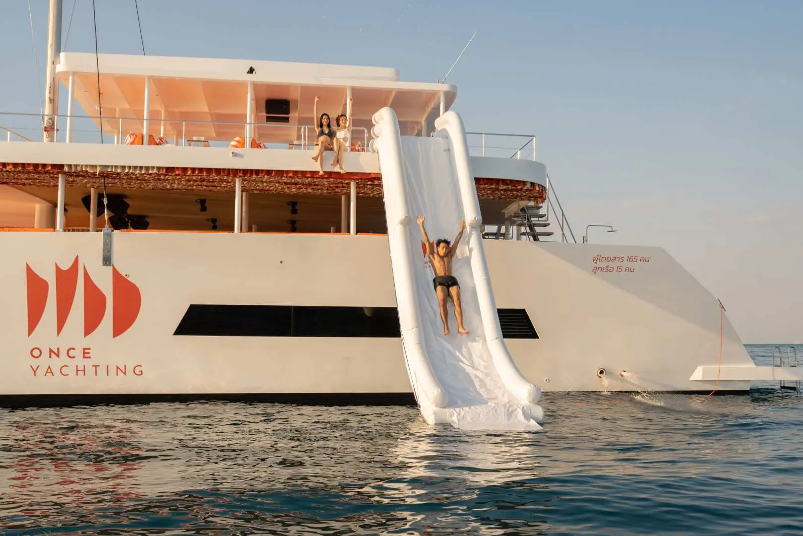 A highlight of the Pattaya catamaran water party, a man slides down a large inflatable waterslide into the ocean, adding thrilling water fun to the three-island hopping tour.
