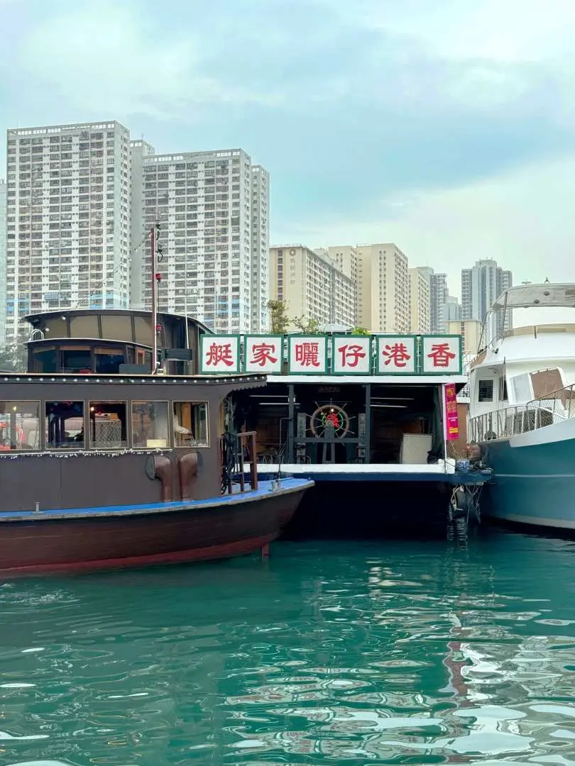 A traditional 'Saai Ga Teng' (曬家艇) houseboat docked in Aberdeen Fishing Village, showcasing the unique living culture of water-dwellers against a modern cityscape backdrop.