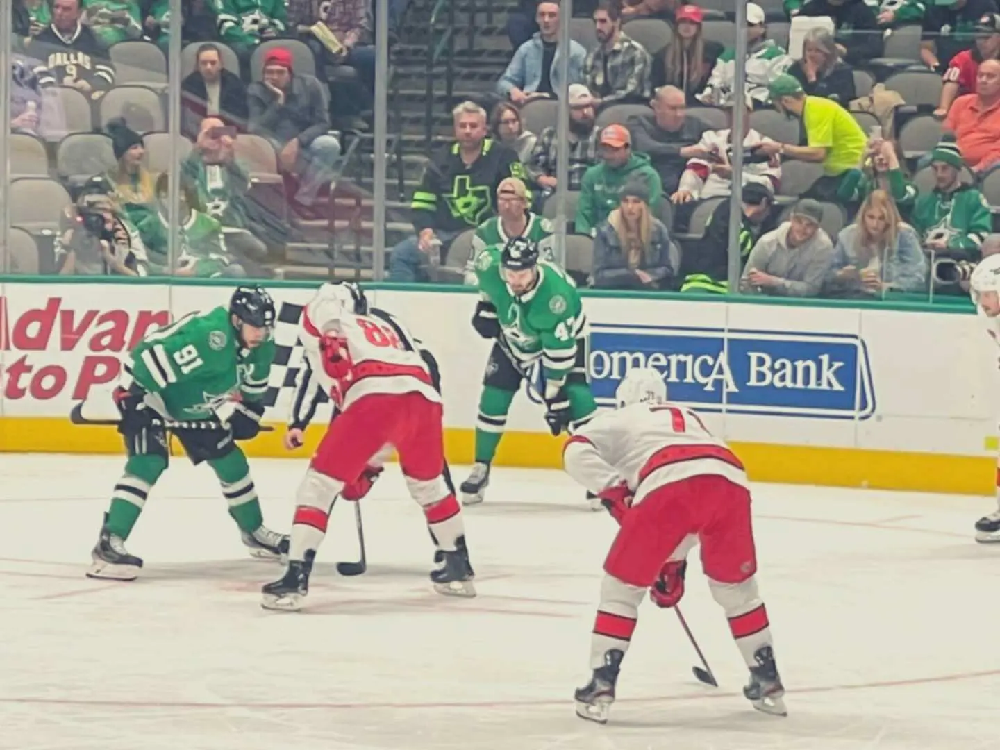 Close-up of Dallas Stars NHL game action, with players in green and red jerseys clashing intensely on the ice, surrounded by cheering fans in the background.