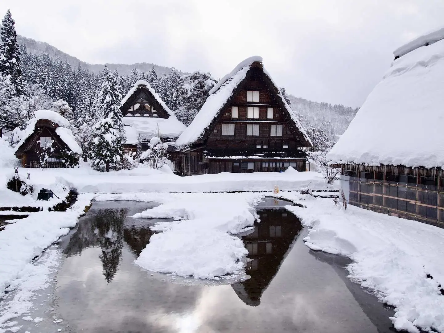 白川鄉冬季雪景，覆蓋白雪的合掌造房屋倒映水面。專業攝影師完美捕捉這世界遺產飛驒高山的夢幻銀白世界。