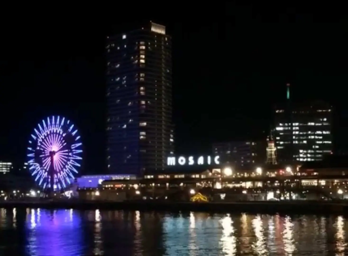 神戶港的璀璨夜景，絢麗的紫色和藍色摩天輪燈光與城市倒影在水面上，營造浪漫氛圍。