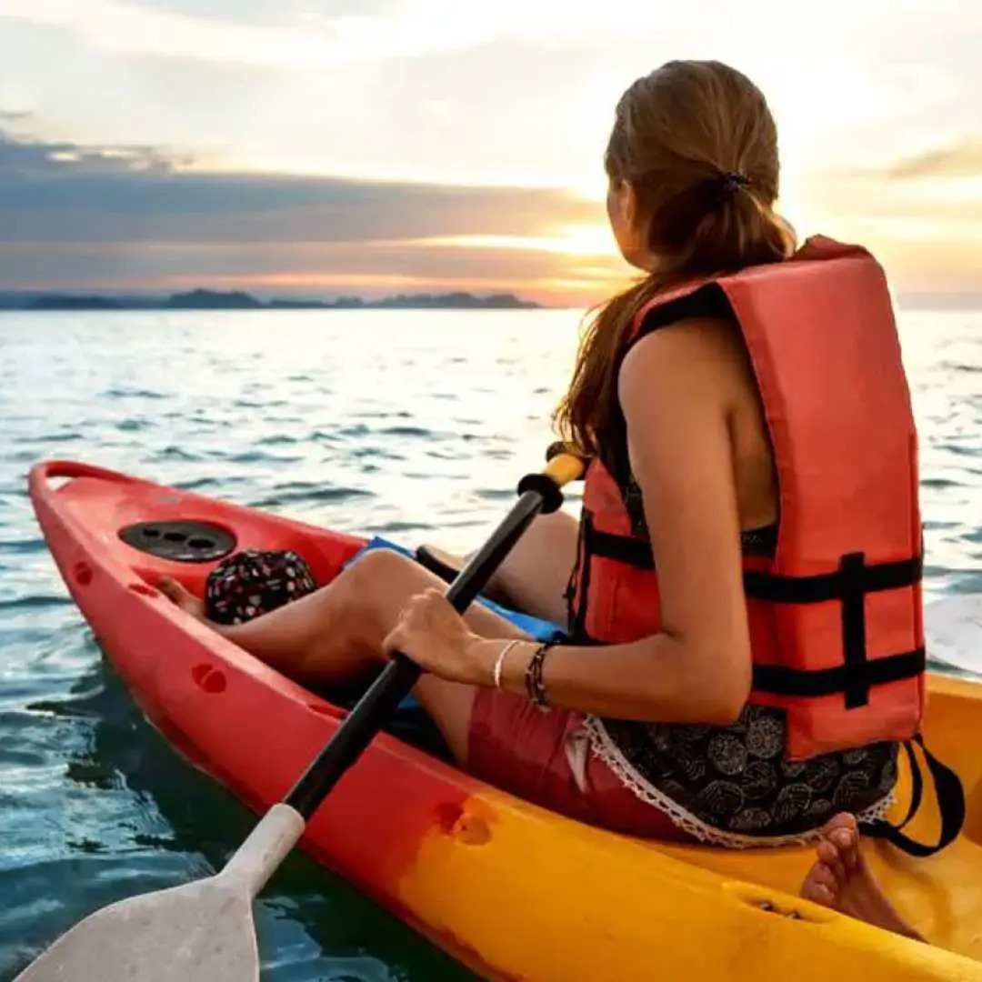 A traveler wearing a life vest sits in a sea kayak at Napaling Reef, Panglao Island, gazing at the sunset over the ocean, enjoying a unique personal experience in the Philippines.