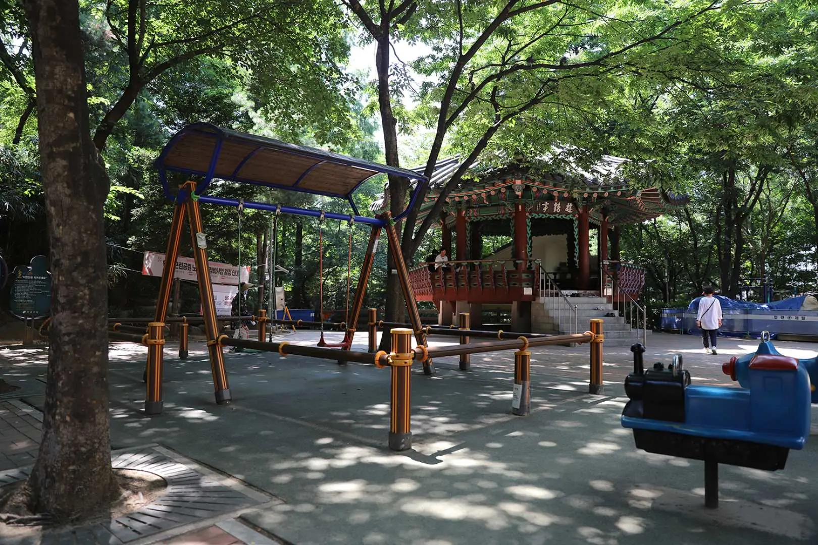 ソウルでのK-POPアイドル聖地巡礼ツアー。公園内には木製ブランコと伝統的な韓屋の東屋があり、ファンがアイドルが休んだであろう場面を想像できる。
