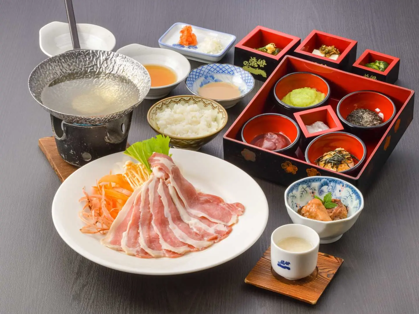 A lavish Iwate mochi and sake shabu-shabu set meal, featuring fresh meat slices, vegetables, and various exquisite side dishes, enjoyed with sake for a unique local culinary experience.