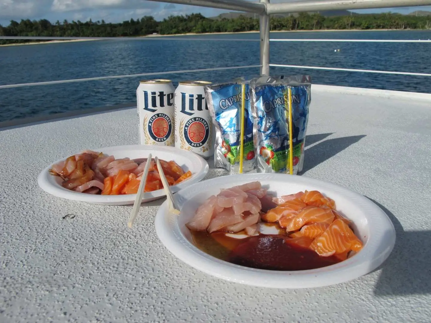 Freshly prepared tuna sashimi plates and cold beverages served on the Guam Princess Dolphin Cruise yacht, offering a delightful onboard dining experience after sea activities.