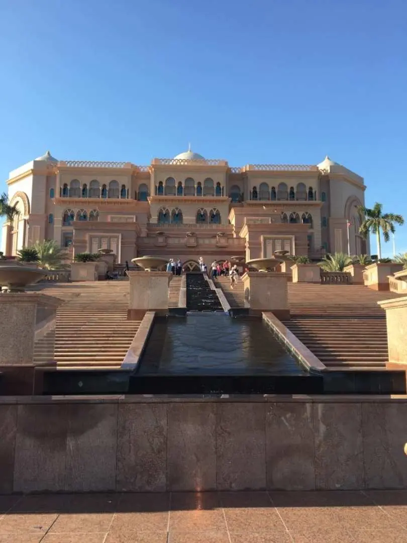 The grand exterior of Emirates Palace Hotel in Abu Dhabi, showcasing its magnificent architecture, cascading fountains, and lush gardens under a clear blue sky, epitomizing luxury.