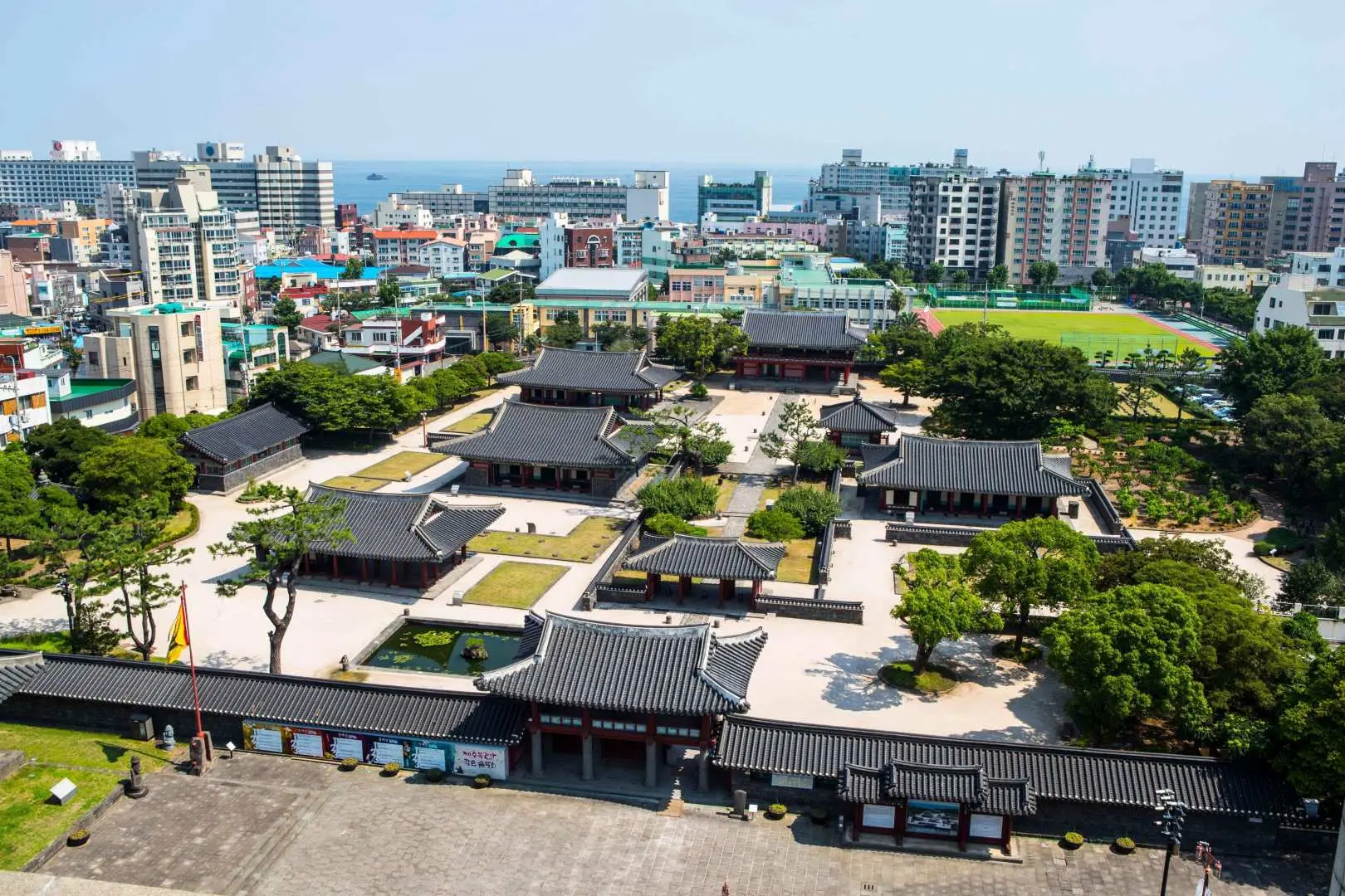 【穿越時空的硃紅印記：在牧官衙與觀德亭，遇見歷史的溫柔】  踏入這片被石牆環繞的古建築群，城市喧囂瞬間被隔絕在朱紅色的木門之外。這裡曾是濟州最高行政機關的所在地，每一片瓦、每一根樑，都浸透了數百年的風霜與故事。而矗立在衙署前的「觀德亭」，那宏偉的單層歇山頂建築，更像是一位沈默的長者，靜靜地守望著這座城市的變遷。  對於韓劇迷而言，這裡是《苦盡柑來》裡那抹帶著苦澀卻又回甘的愛情縮影。漫步在古色古香的長廊下，看著陽光穿透欞窗，在磨光的木地板上灑下斑駁的光影，你彷彿能看見劇中主角在此徘徊的身影。這裡的每一處轉角，都像是被刻意安排好的分鏡，讓人忍不住想停下腳步，屏息感受那份時空交錯的浪漫。