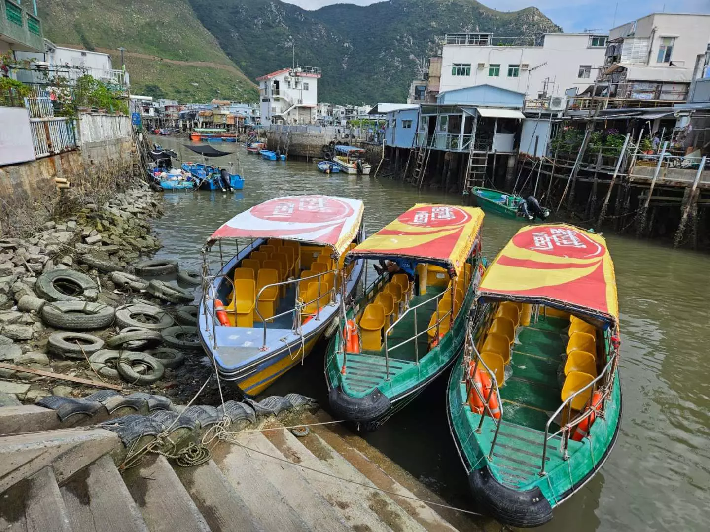 Three vibrant sightseeing boats docked in Tai O's tranquil stilt house village, offering scenic tours through the 'Venice of Hong Kong' waterways, showcasing its unique charm.