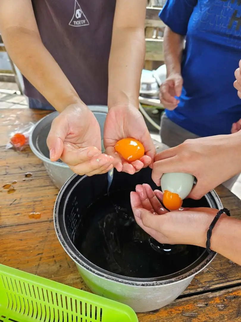 Close-up of participants' hands preparing salted duck eggs, holding vibrant orange yolks and rinsing eggs, experiencing the traditional food crafting in Tai O.