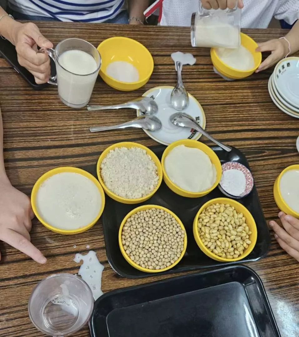 Participants gather around a table with bowls of soybeans, rice, and fresh soy milk, actively engaged in the hands-on process of making traditional Tai O tofu pudding.