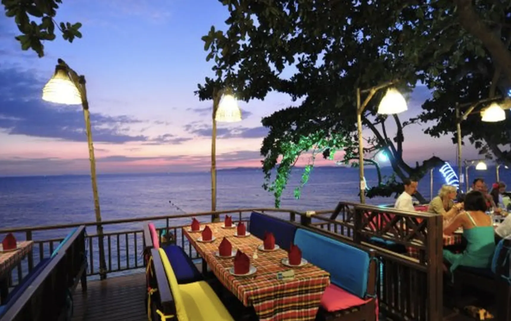 ร้านอาหารกะหล่ำปลีและถุงยางอนามัยพัทยาช่วงพระอาทิตย์ตกดิน โซนรับประทานอาหารริมระเบียงที่มองเห็นวิวทะเลสวยงาม มีโต๊ะจัดเตรียมไว้สำหรับแขกที่มาเพลิดเพลินกับบรรยากาศยามค่ำคืน