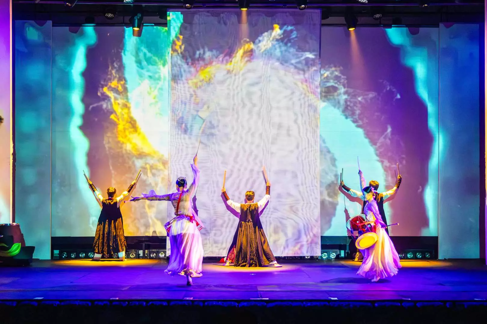 Jeju Island K-show's vibrant Korean traditional dance, with five dancers in flowing costumes performing on stage, against an abstract and colorful dynamic projection, creating a visual feast.