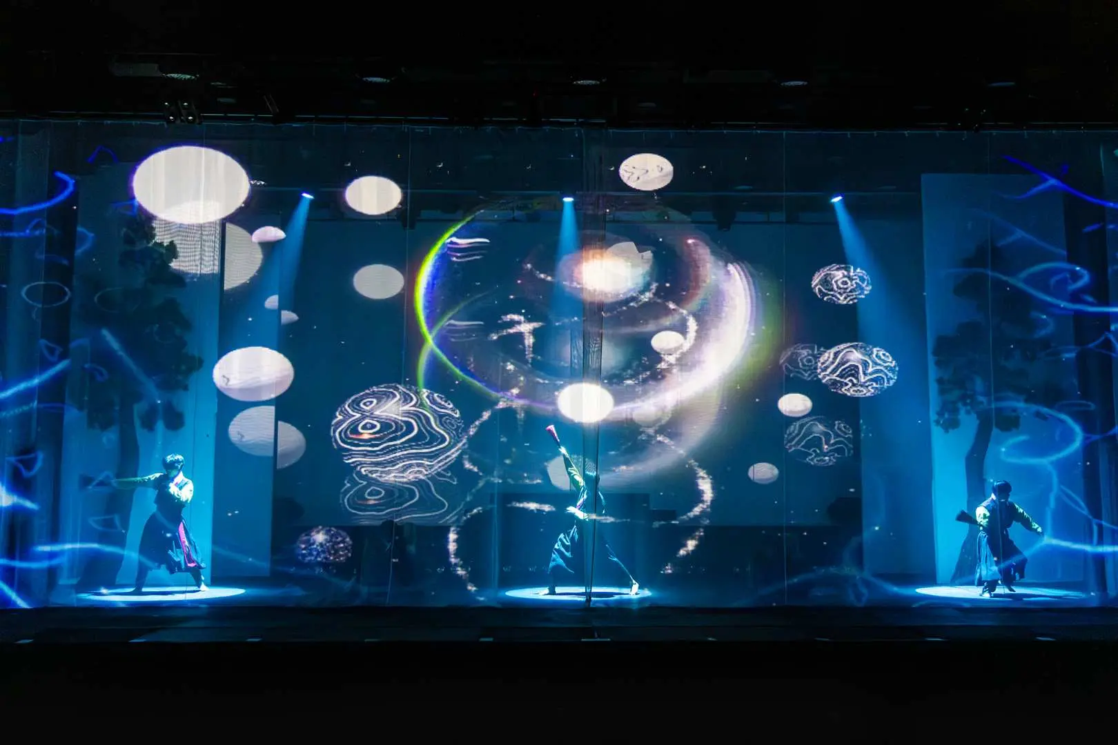 Jeju Island K-show's LED technology light and shadow performance, with blue and white glowing rings and floating spheres projected on stage, where two performers create a sci-fi visual effect, showcasing modern artistic charm.