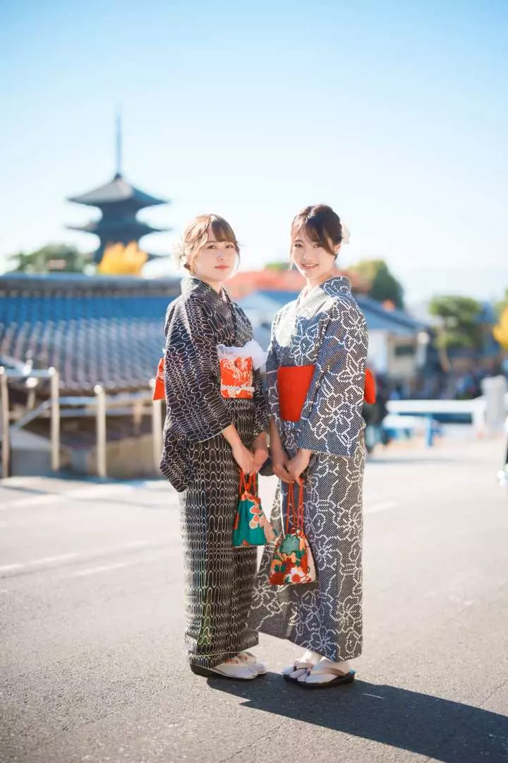 两位身穿优雅花纹浴衣的女性在京都传统宝塔前合影，展现和服租赁与专业摄影师拍摄的闺蜜旅行美好时刻。