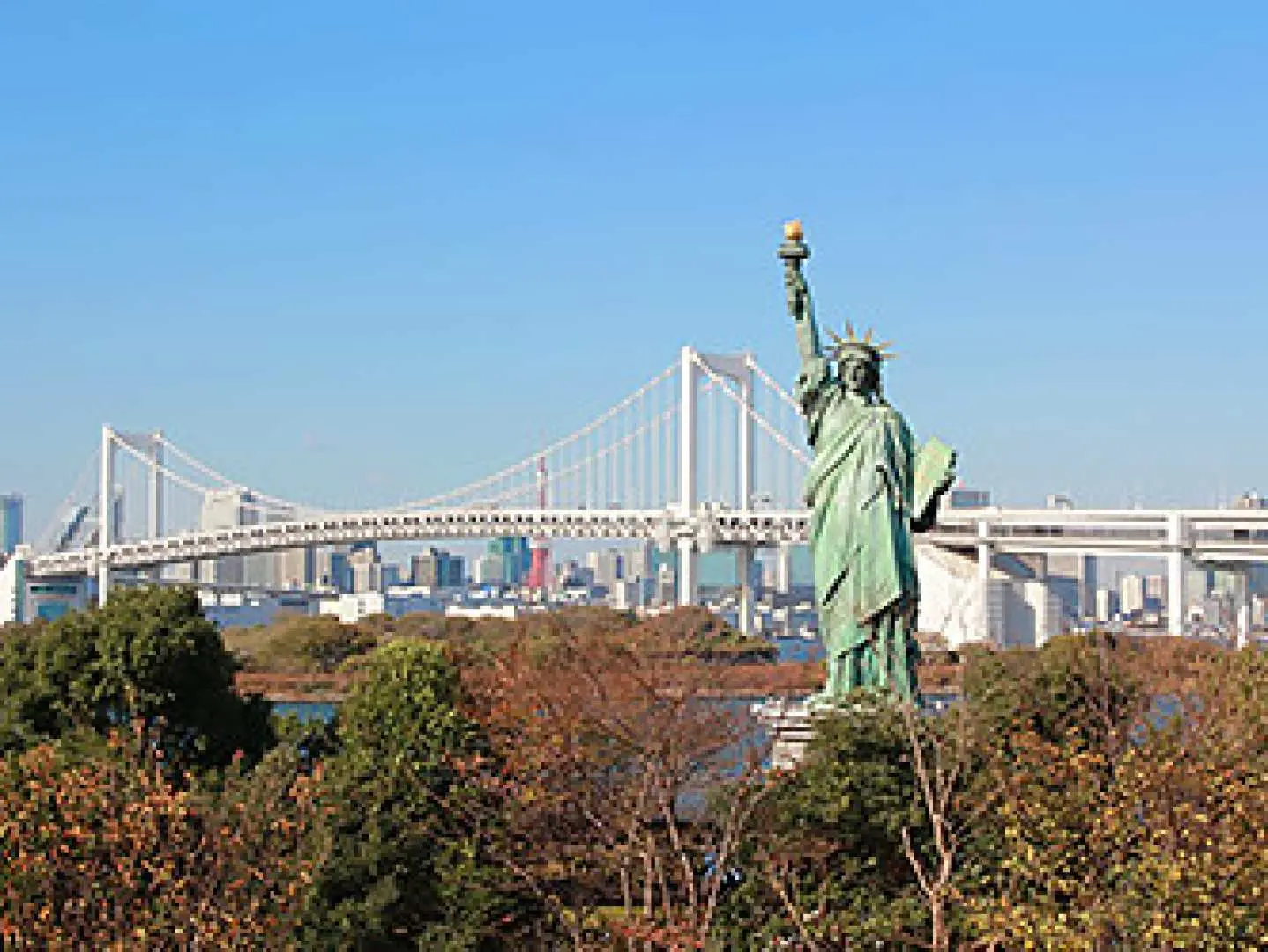 台場自由女神像傲然矗立，背景是東京標誌性的彩虹大橋與都市天際線，是東京灣區的絕佳拍照打卡點。