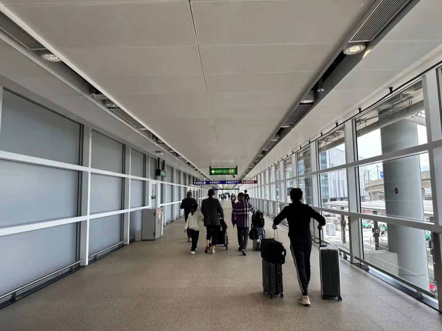香港國際機場內明亮的旅客通道，多位旅客正拖著行李行走，前往機場接送服務的會合點，展現便利的動線。