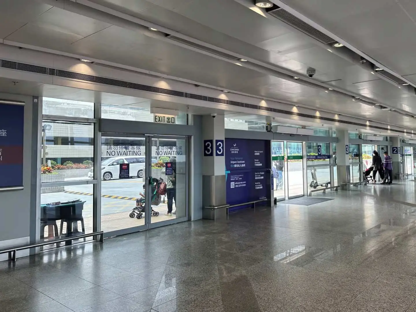 香港國際機場的33號出口，明亮的玻璃門外可見等候區，指示旅客前往機場接送服務的上車點。