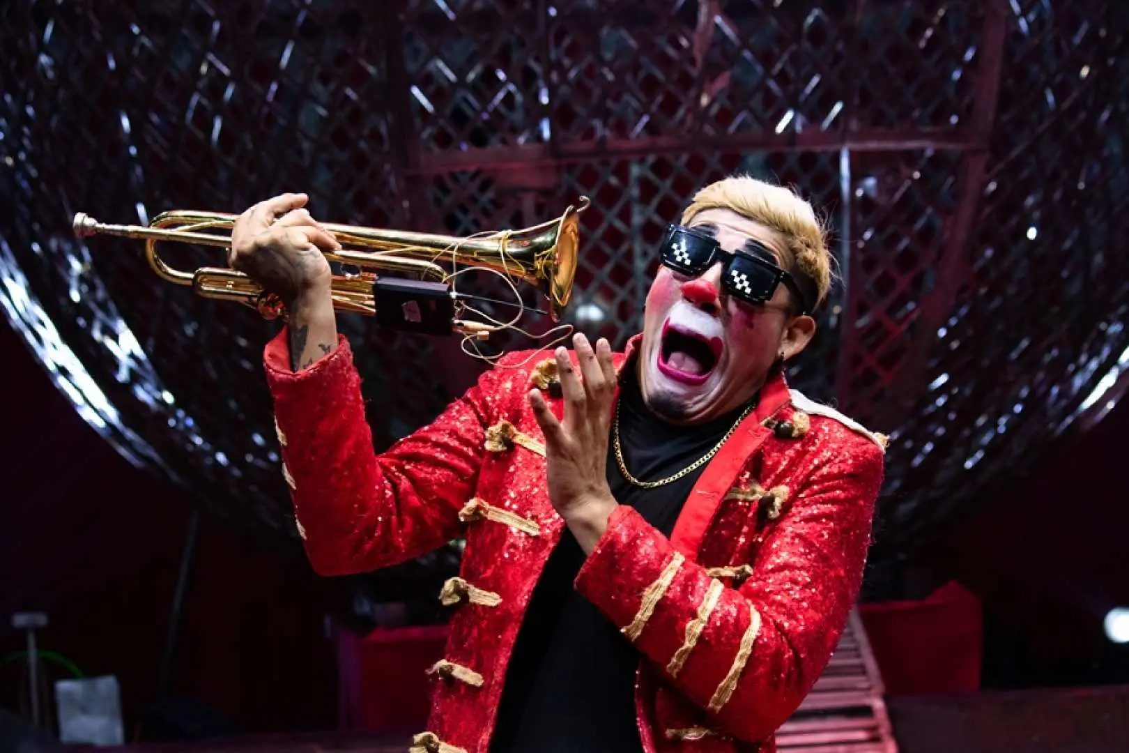At Taichung Houli Crazy Horse Circus's Magic Bubble Fun World, a quirky clown in a sparkly red suit and sunglasses plays a trumpet, bringing joy to the audience.